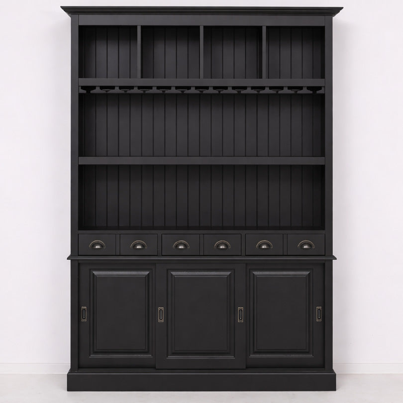 Vaisselier en bois peint noir vu de face avec partie haute ouverte composée de compartiments et étagères, porte-verres intégré sous une étagère, rangée de tiroirs au centre et partie basse fermée par trois portes pleines.