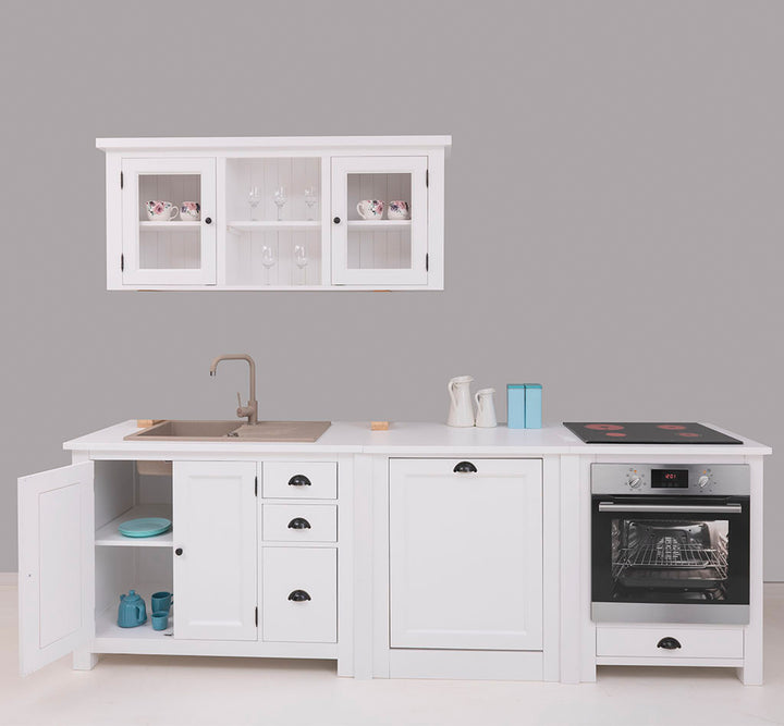 Aménagement de cuisine complet en bois blanc comprenant un meuble sous-évier avec porte ouverte, un module central, un bloc four avec plaque de cuisson et un élément mural haut avec portes vitrées laissant apparaître de la vaisselle.