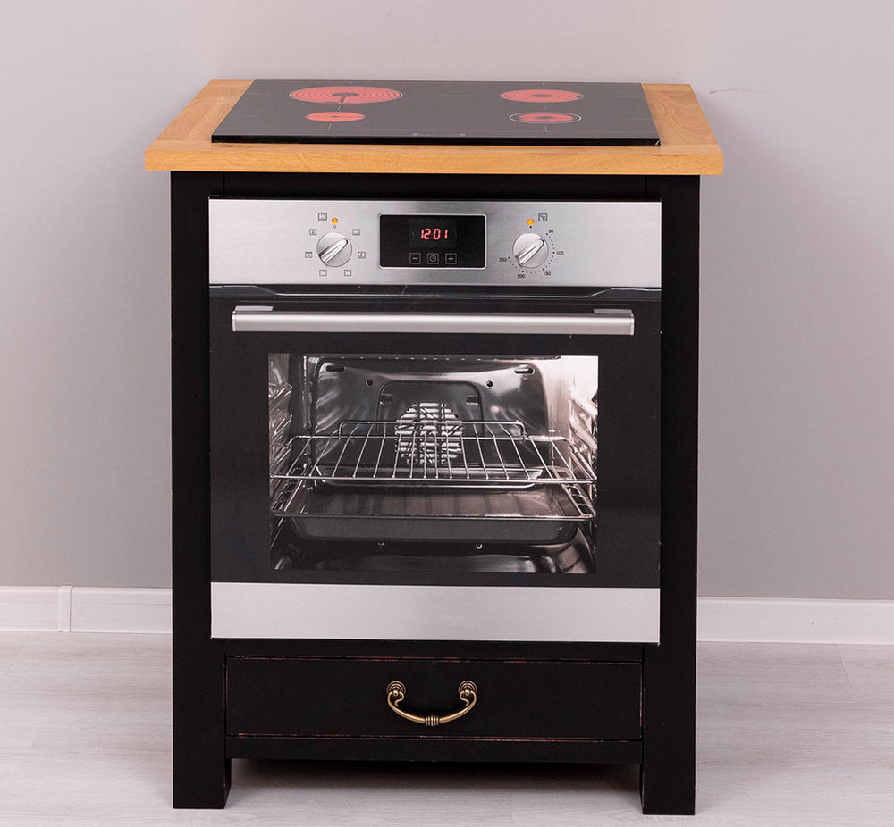 Vue de face d'un meuble de cuisine noir avec plan de travail en bois clair massif, équipé d'une plaque de cuisson vitrocéramique à quatre foyers et d'un four encastrable avec intérieur visible, situé au-dessus d'un tiroir à poignée vintage dorée.