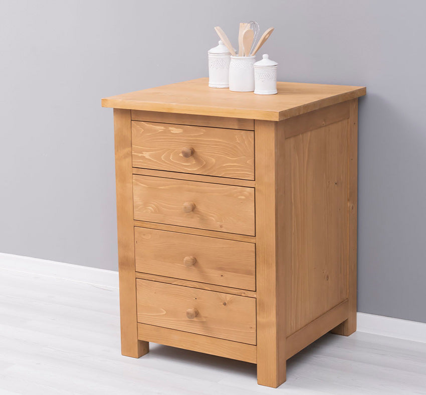 Petite commode en bois clair avec quatre tiroirs et boutons de préhension ronds, disposée contre un mur gris avec des ustensiles et pots de cuisine sur son plateau.