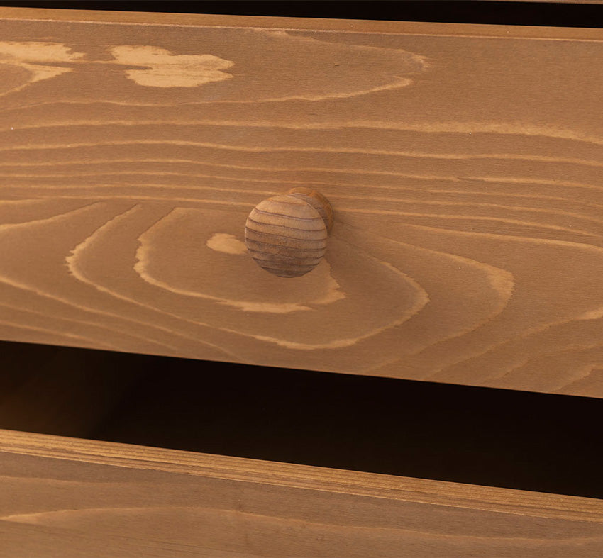 Gros plan détaillé sur un bouton de tiroir rond en bois et le veinage naturel du bois clair sur la façade du meuble.