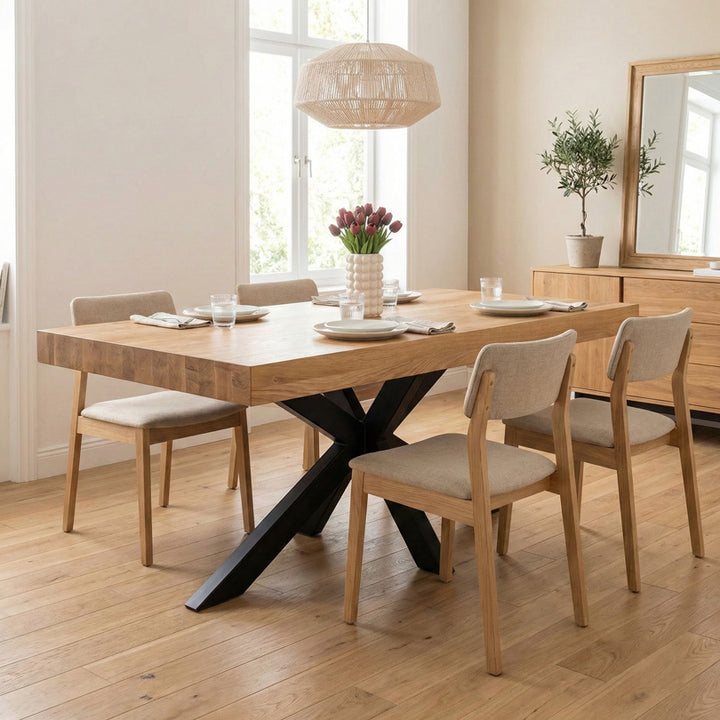 Table en chêne massif avec plateau épais et pied central en métal noir, présentée dans une salle à manger avec chaises.
