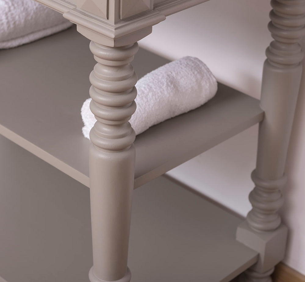 Zoom sur le pied tourné artisanal et l'étagère de rangement d'un meuble de salle de bain en bois peint gris galet.
