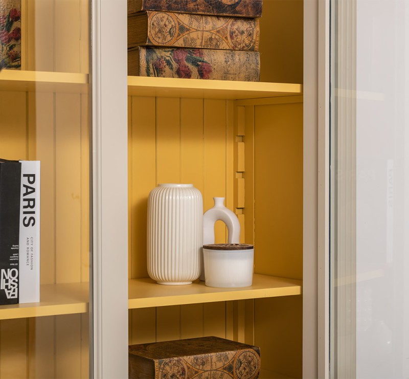 Détail de l’intérieur d’une bibliothèque en pin massif style Directoire avec étagères jaunes derrière porte vitrée