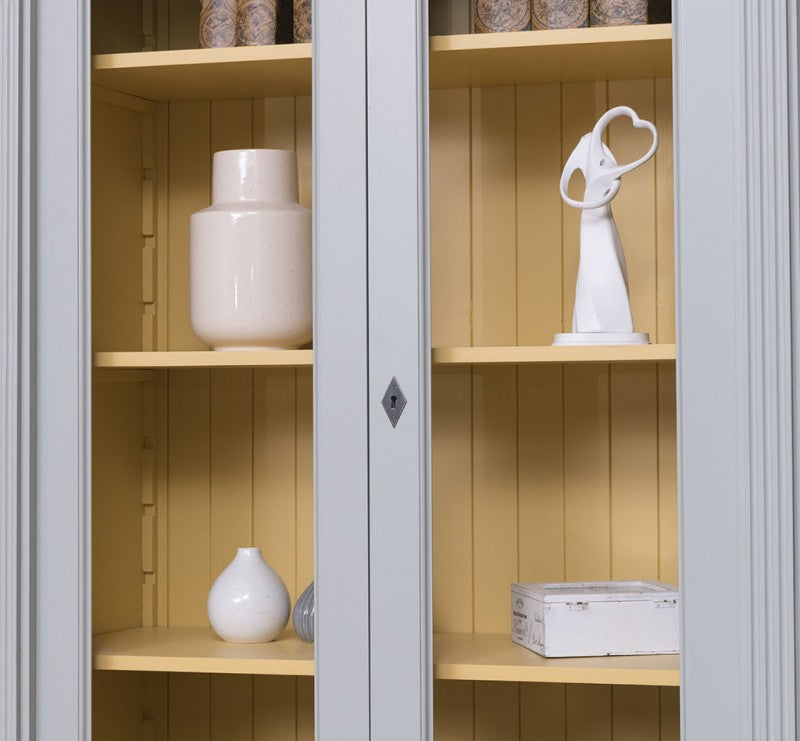 Détail d’une porte vitrée fermée avec intérieur jaune à lames d’une bibliothèque en pin massif style Directoire