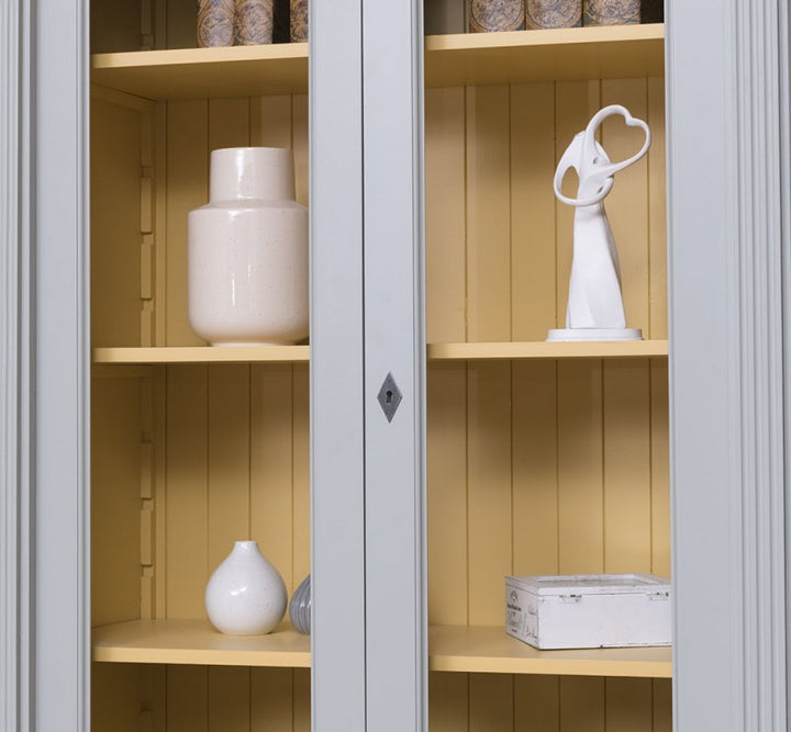 Détail d’une porte vitrée fermée avec intérieur jaune à lames d’une bibliothèque en pin massif style Directoire
