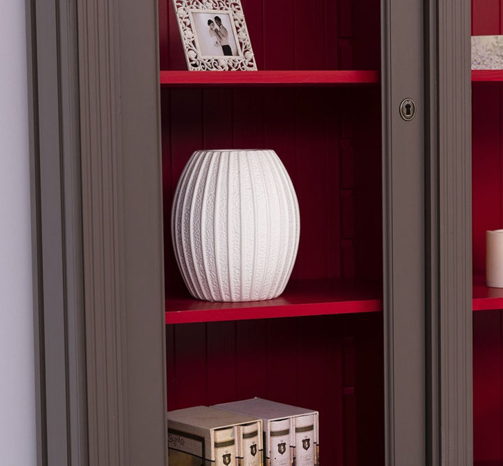 Détail de l’intérieur rouge d’une bibliothèque style Directoire avec étagère rouge et vase blanc derrière montants gris